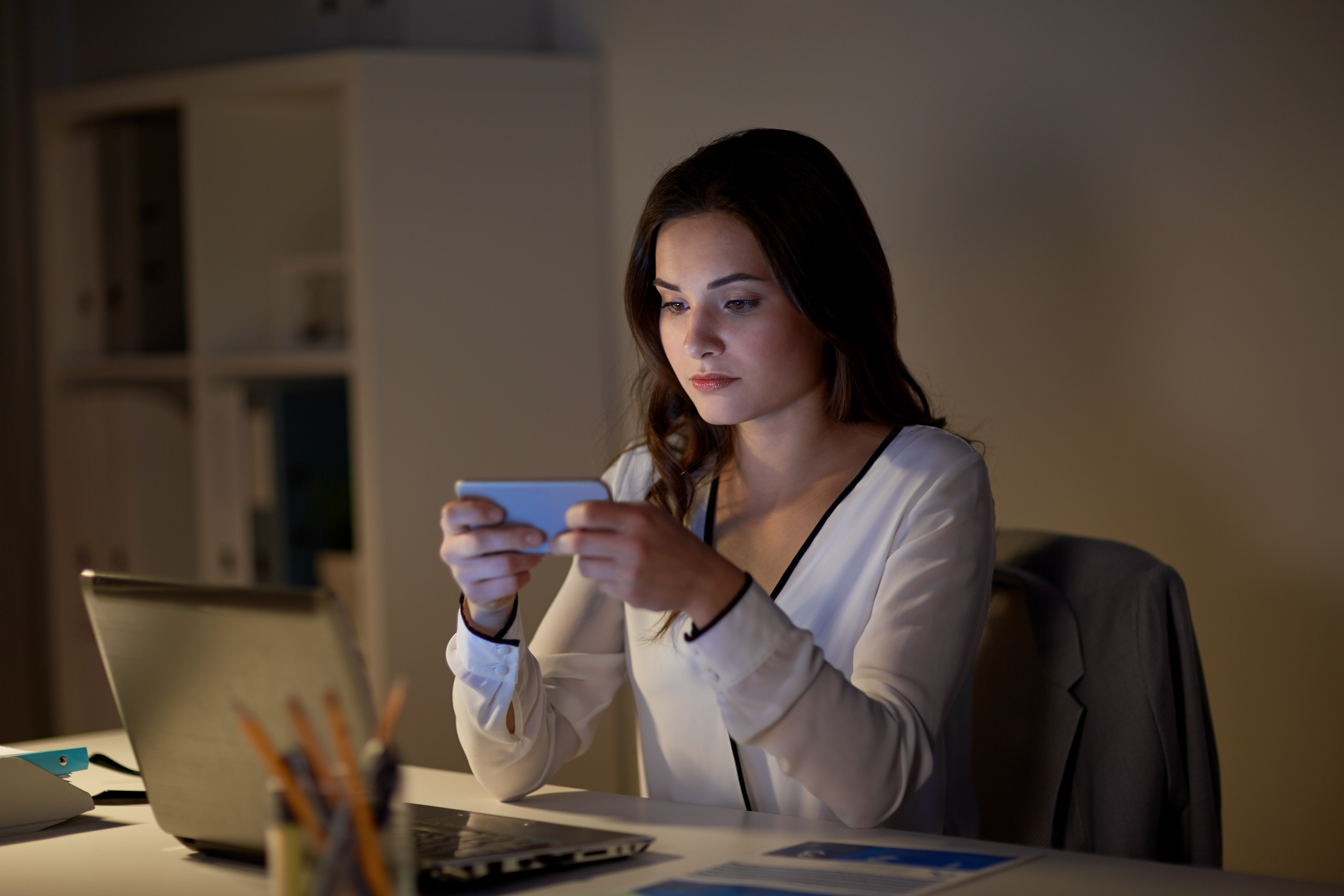 Professional reviewing promotional messaging on smartphone while working on laptop